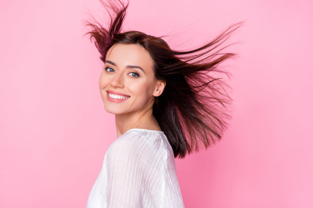 年轻女性的照片肖像，健康完美的头发，穿着时尚的白色服装，背景为粉色，宣传护发产品。图片下载