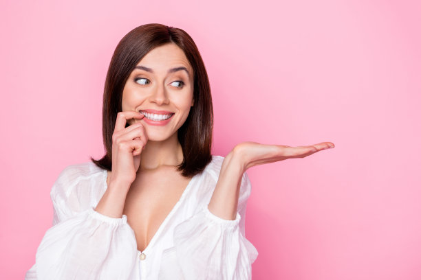 年轻女士咬指甲，拿着美味的文案宣传品，身穿时尚白色服装，粉色背景照片图片下载