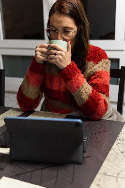 身穿毛衣的女人一边喝茶，一边在平板电脑上看电影图片下载