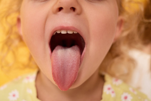 金发卷发幼儿特写，做出搞怪表情，调皮地吐舌头，表现得有趣而顽皮，站在黄色背景下的室内。图片下载