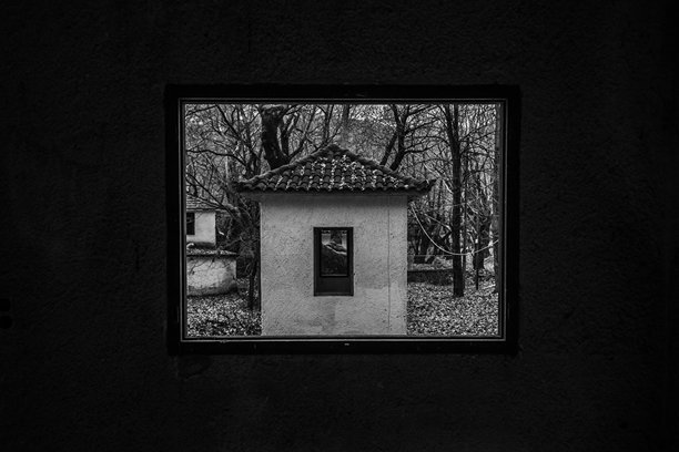 一幅黑白图像，透过另一座废弃房屋的窗户框住的废弃房屋。图片下载