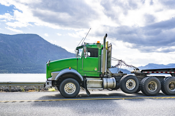 绿色大驾驶室重型半挂卡车，搭载步台半挂车，在阳光明媚的日子里沿着哥伦比亚河行驶。图片下载