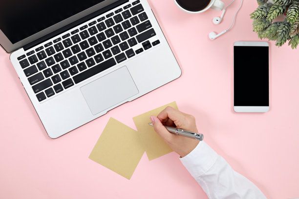 从上方直接拍摄的女商人在粉色背景下的笔记本电脑旁写便签图片下载