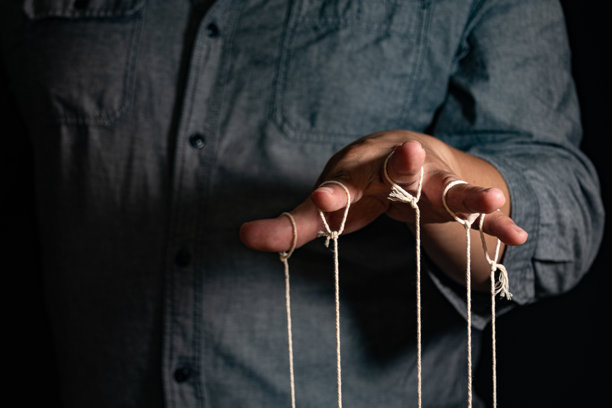 特写镜头：男人用手指操控木偶。男人的手通过与线相连的手指控制木偶，背景为黑色，体现操控的概念。图片下载