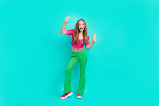 兴奋可爱的女学生穿着粉色短款上衣和喇叭裤在青绿色背景下跳舞玩得很开心的全身照片图片下载