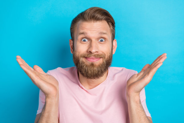 穿着粉色T恤、举起手臂耸肩的时尚、疑惑的年轻男人，蓝色背景照片图片下载