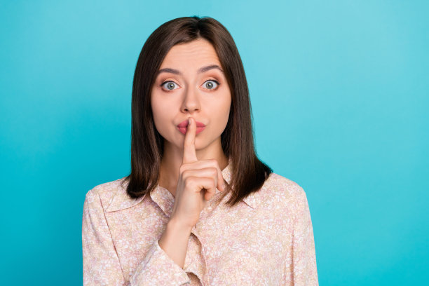 特写照片，年轻漂亮的女性用手指触碰嘴唇，保持秘密，穿着时尚休闲的服装，背景为水绿色。图片下载