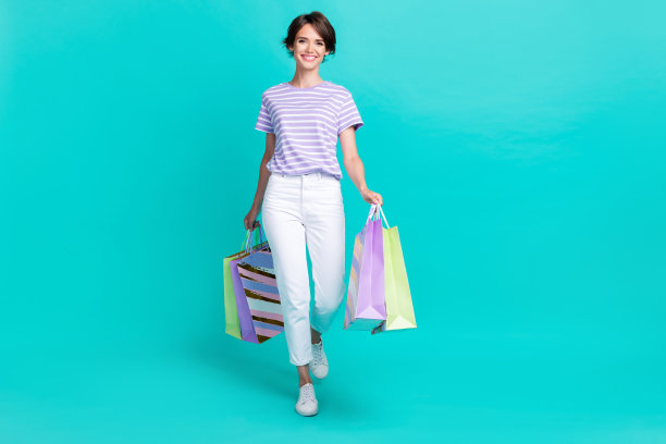 穿着紫色T恤的甜美迷人女士在土耳其蓝色背景下走路，手里提着购物袋的全身照片图片下载