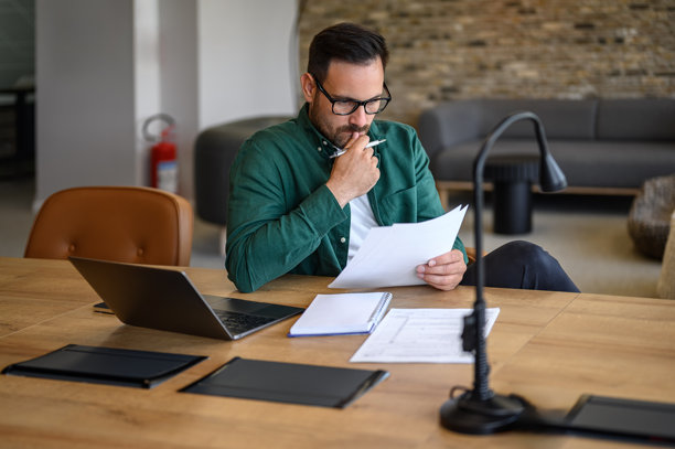 专注的男企业家戴着眼镜，在办公室的桌子上分析商业报告。图片下载
