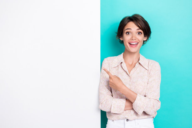 一位留着印象深刻的波波头女士，穿着白衬衫和牛仔裤，独自站在青绿色背景前。图片下载