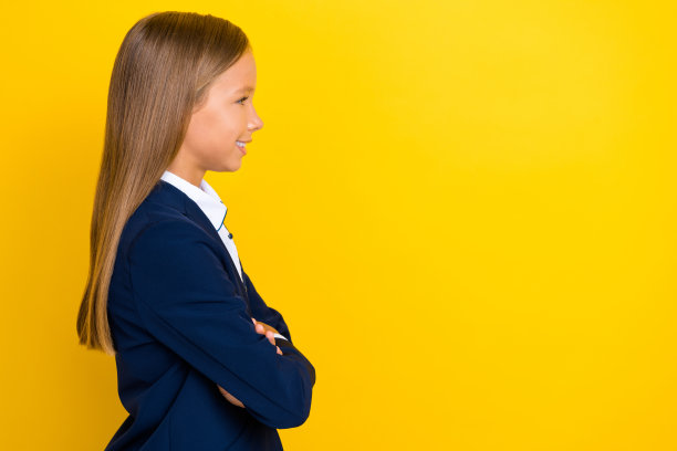 可爱的女孩侧面照片，双臂交叉，穿着时尚的衣服，望向空旷的教室，背景为黄色。图片下载