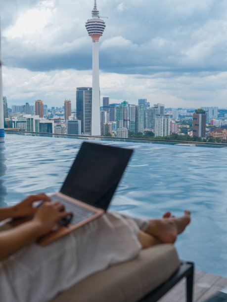 在泳池边使用笔记本电脑的女性，俯瞰吉隆坡的美景图片下载