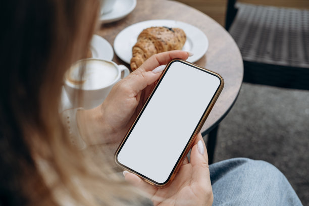 咖啡店内，女性手持白色空白屏幕的智能手机，适用于移动应用设计和广告，在线营销。图片下载