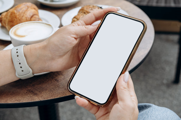 咖啡店里，女性手持白色空白屏幕的智能手机，适用于移动应用设计和广告，在线营销。图片下载