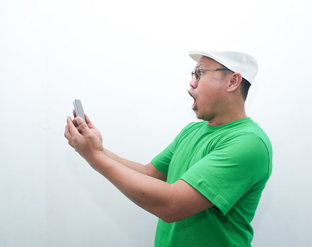 一位亚洲男子手持手机，面露震惊表情的照片图片下载