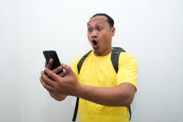 一位亚洲男子手持手机，面露震惊表情的照片图片下载