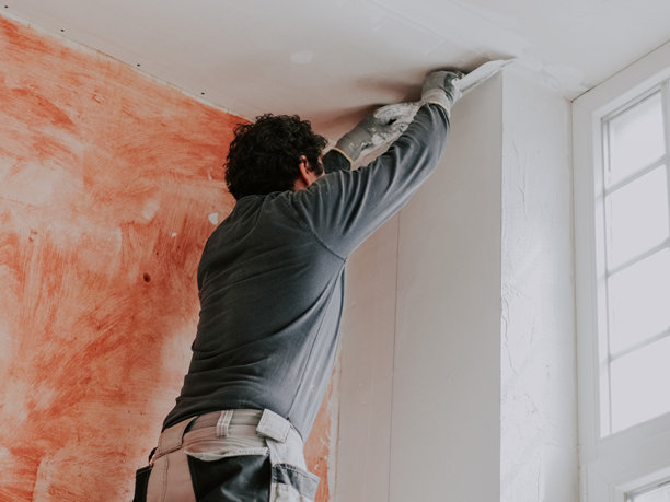 一位白人年轻男子正在墙上涂抹腻子。图片下载