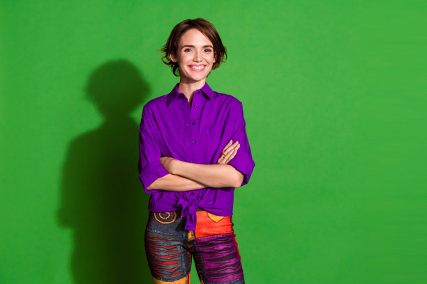 自信迷人的复古风格年轻女孩肖像照片，穿着紫色衬衫，双手交叉，背景为绿色。图片下载