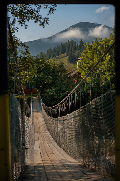 美丽的悬索桥横跨喀尔巴阡山脉的一条山间河流，远处山峦笼罩在雾气中，富有氛围的照片图片下载