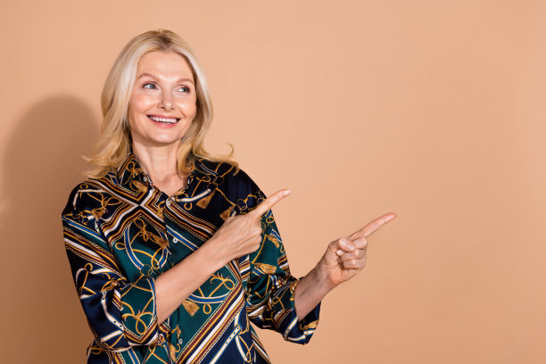 金发女销售员的照片肖像，穿着华丽的衬衫，手指指向空白区域，背景为米色。图片下载