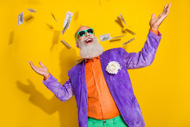 穿着色彩鲜艳服装的积极古怪的富翁爷爷，开心地在黄色背景下挥舞美元钞票。图片下载
