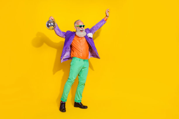 快乐无忧的爷爷手持迪斯科球，享受乐趣，背景为黄色。图片下载