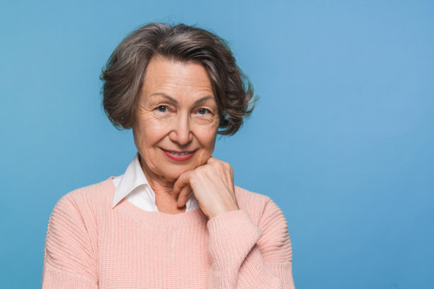 美丽的退休女性微笑着抚摸下巴，穿着休闲服装，背景为蓝色。图片下载