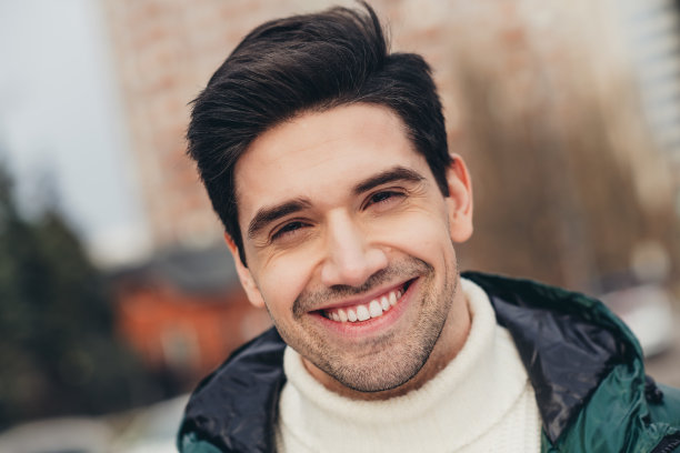 特写照片：一位帅气、愉快的男人在寒冷的秋季天气中走在城市街道上。图片下载