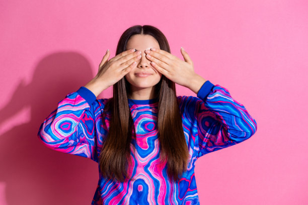 时尚多彩服装的迷人少女在粉色背景下遮住眼睛玩捉迷藏的照片肖像图片下载