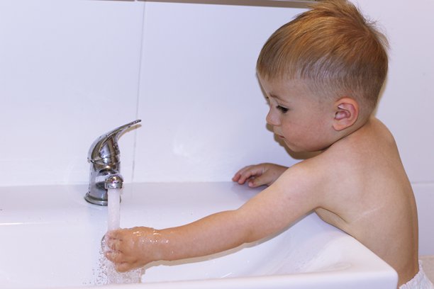 一个小孩在浴室里自己伸手去开水龙头。图片下载