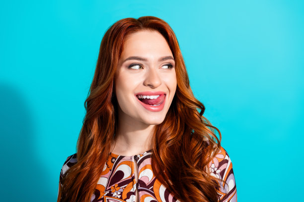 可爱的年轻女士的照片肖像，舔着牙齿，目光空洞，穿着时尚的彩色服装，背景为青色。图片下载