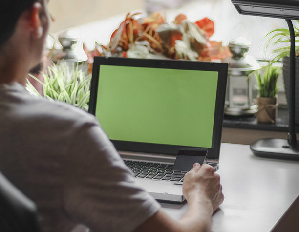 坐在带有绿屏笔记本电脑的房间里进行网上购物的年轻白人男子图片下载