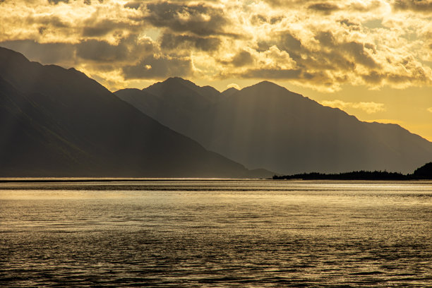 阿拉斯加安克雷奇附近的特纳根湾晚下午风景照片。山脉呈剪影，金色的阳光在水面上反射。图片下载