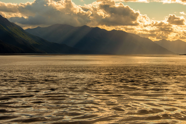 阿拉斯加安克雷奇附近的特纳根湾晚下午风景照片。山脉呈剪影，金色的阳光在水面上反射。图片下载