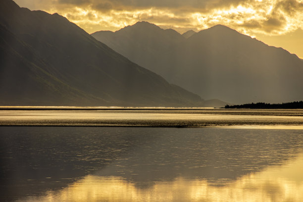 阿拉斯加安克雷奇附近的特纳根湾晚下午风景照片。山脉呈剪影，金色的阳光在水面上反射。图片下载