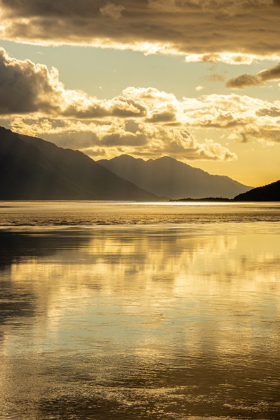 阿拉斯加安克雷奇附近的特纳根湾晚下午风景照片。山脉呈剪影，金色的阳光在水面上反射。图片下载