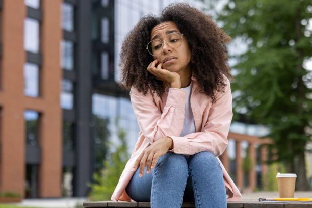 年轻女子在户外感到无聊或悲伤，坐在城市公园的长椅上图片下载