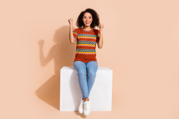 大喜的女人穿针织t恤牛仔裤坐在立方体尖叫是的赢得彩票孤立米色背景的全尺寸照片图片下载