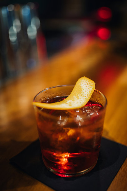 水晶杯中的尼格罗尼鸡尾酒，配有橙片和新鲜生橙，置于酒吧内。图片下载