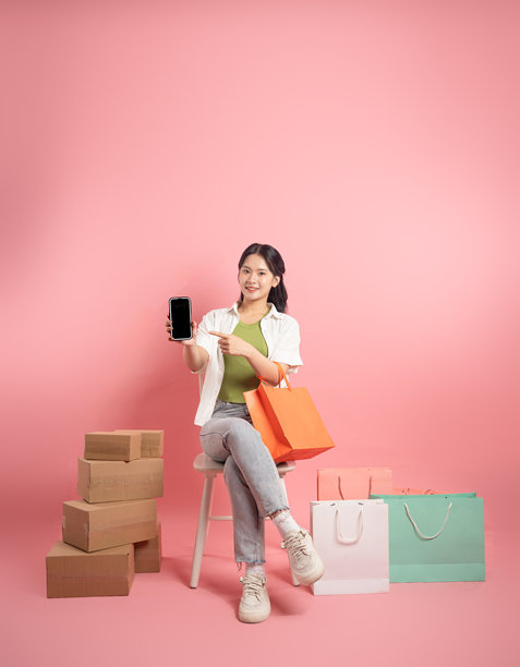 亚洲女性在粉色背景前摆姿势，旁边有购物袋图片下载