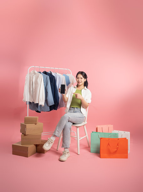 亚洲女性在粉色背景前摆姿势，旁边有购物袋图片下载