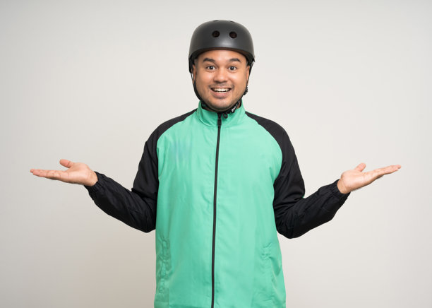 年轻的亚洲骑手穿着绿色夹克制服和骑行头盔，在白色背景上展示各种动作。男性送餐服务工作人员。送货快递员和食品配送服务。图片下载