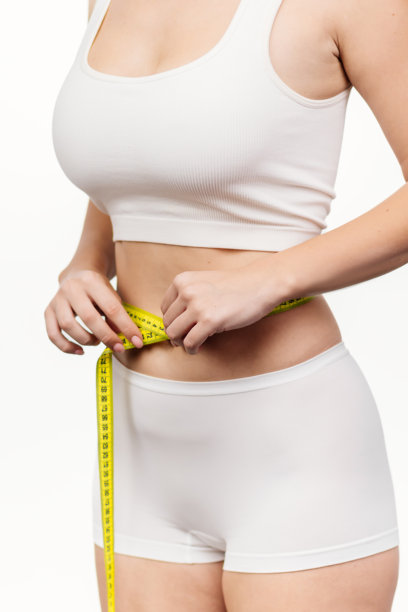 一位纤细的女孩用卷尺测量她的腰围。这个瞬间突显了女性身材的美丽，并强调了对健身和身体护理的关注。图片下载