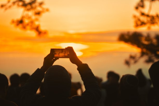 人影在智能手机上拍摄日出，迷人的黄金时刻摄影，热爱日出的自然爱好者，适用于旅行博客、冒险旅游和户外生活方式的库存图片。图片下载