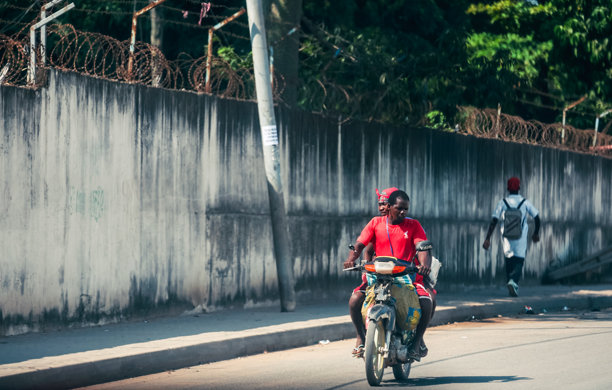 两名男子在安哥拉罗安达的繁忙街道上骑摩托车，正值白天。图片下载
