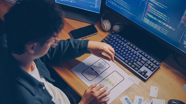 UX开发者在深夜加班，特写镜头展示他在纸质原型上排列移动应用UI/UX设计元素，正在制作线框图或纸质原型。图片下载