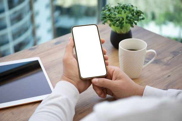 男性手握着手机，背景为白色桌面，手机屏幕为孤立状态。图片下载