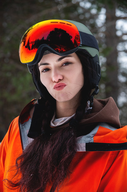 穿着滑雪服和装备的女性滑雪者或单板滑雪者站着对着镜头做搞笑表情。极限冬季运动在度假村进行。图片下载