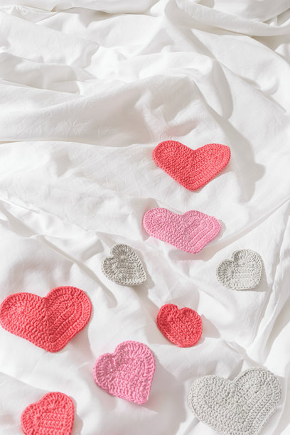 粉红色手工编织的情人节心形装饰放在白色床单上。极简生活方式的舒适照片，情人节，浪漫，爱情，婚礼概念，俯视美学静物，创意图案。图片下载