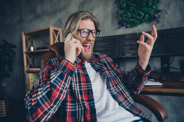 一位金发年轻商人在共享办公空间的扶手椅上坐着，手持智能手机，正在进行电话通话，显得有些紧张。图片下载